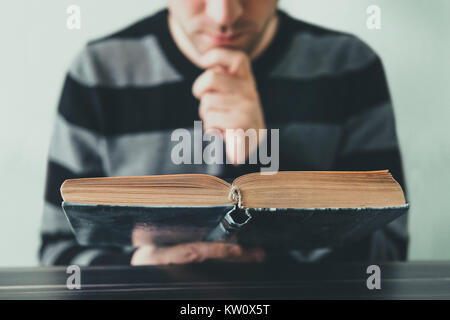 Young man opening and reading a book, close up. Young adult carefully, thoughtfully reading a book sitting at the Desk in the library Stock Photo