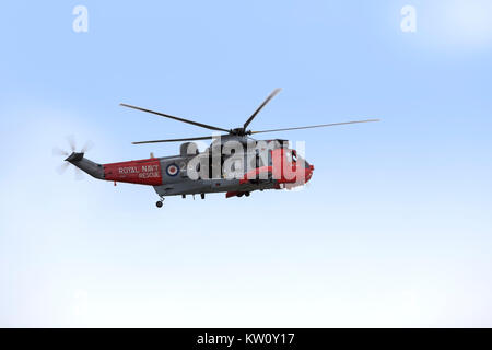 Royal Navy Sea King helicopter on a rescue exercise under a hazy blue sky Stock Photo