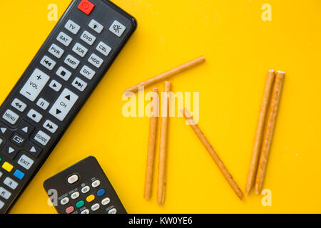 Weekend, hobby and leisure concept. A TV inscription made of bread sticks and remote controls on a bright one-colore yellow background. Close up. Spac Stock Photo