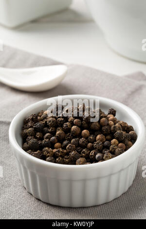 Raw, natural, unprocessed black pepper peppercorns white bowl on kitchen table Stock Photo