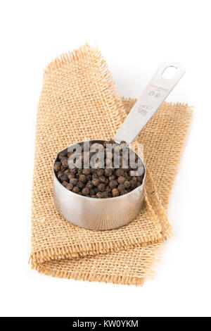 Raw, natural, unprocessed black pepper peppercorns in measuring cup on white background Stock Photo