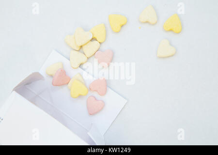 Veterinary and animal healthcare concept. Curing pets. Pink and yellow heart shaped pills pouring out of a white box, close up, white background.Space Stock Photo