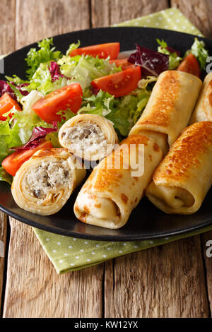 Crepes with chicken and mushrooms close-up on a table and salad of fresh vegetables. Vertical Stock Photo