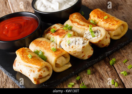 Pancakes rolls stuffed with chicken and mushrooms close-up and tomato sauce, sour cream on the table. horizontal Stock Photo