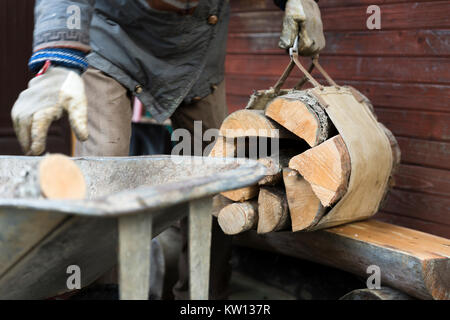 Man collecting firewood in basket from wheelbarrow Stock Photo