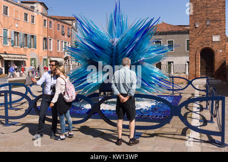 Tourists posing in front of the spectacular 'Comet Glass Star' sculpture on the island of Murano, Venice Stock Photo