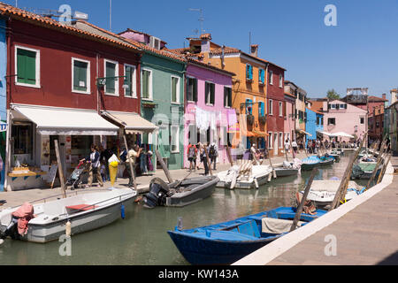 Tourists walking along the main canal in Burano and enjoying the colourful homes it is famous for Stock Photo