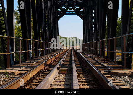 Empty train tracks on a bridge taken from a low angle, blue sky, forest at end Stock Photo