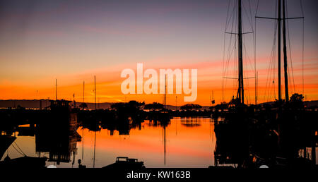 A blazing sunset reflects in marina water with silhouettes of sail boats and their masts. Stock Photo