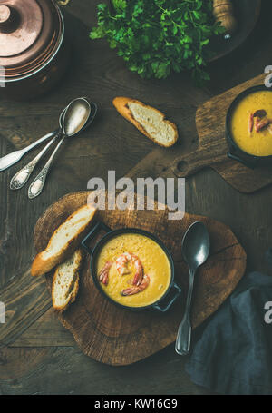 Flat-lay of corn creamy soup with shrimps served in individual pots with bread over rustic dinner table, top view. Slow food, winter warming food conc Stock Photo