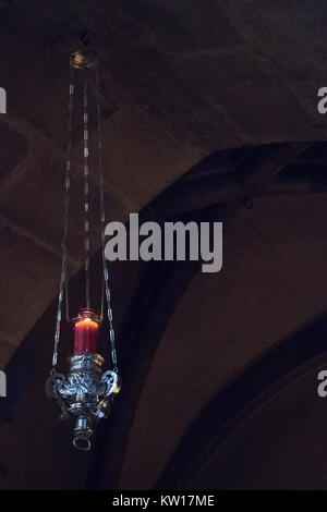 A red candle in a silver candle holder hanging suspended from stone arches. Stock Photo