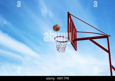 Old Basketball ring on blue sky background with ball into a basket. Stock Photo