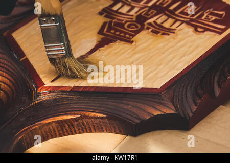 man paints a wooden box. cost covers the Lakme wooden Board with hand carved. Handmade on wood. Lacquered kitchen utensils. Old Russian Ukrainian Slav Stock Photo