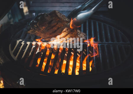 Upturning of fried steak on grill pan, closeup. Big raw piece of meat from beef to black metal lattice for frying Stock Photo