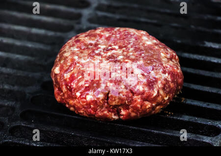 Raw Beef Patty for Burger on black hot grill. Raw Patty of fresh ground beef. The process of making the toppings for a Burger Stock Photo