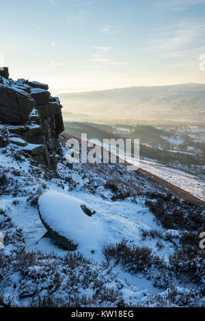 Dawn at Bamford edge in the Peak District on a cold winter morning. An old abandoned millstone covered in snow. Stock Photo