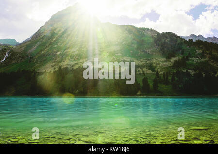 Bright sunlight shines from behind the mountain. The rays of the sun on a mountain lake. Stock Photo