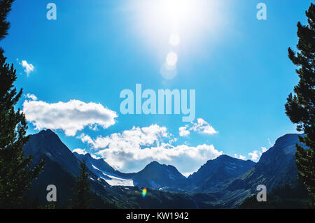 top of mountains in blue sky. The sun shines brightly over the top of a high mountain on the background blue beautiful sky with white clouds Stock Photo