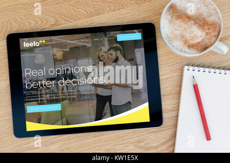 The Feefo website on an iPad tablet device which rests on a wooden table beside a notepad and pencil and a cup of coffee (Editorial only) Stock Photo