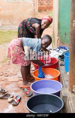 Lugazi, Uganda. June 09 2017. Young African girls washing laundry in washbasins in front of a house. Stock Photo
