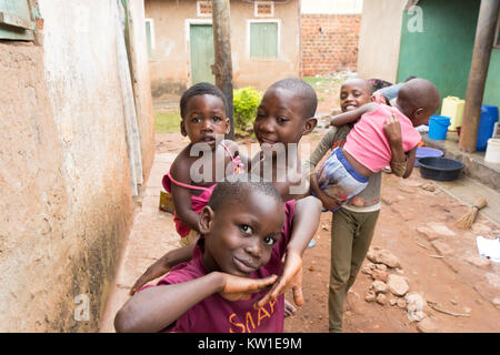 Lugazi, Uganda. June 09 2017. Young African boys holding their siblings in their arms. Girls in the background are washing laundry in basins. Stock Photo