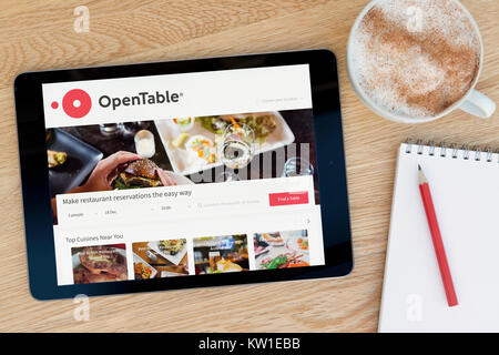 The Open Table website on an iPad tablet device which rests on a wooden table beside a notepad and pencil and a cup of coffee (Editorial only) Stock Photo