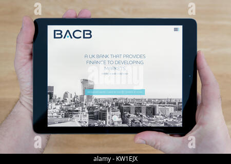 A man looks at the British Arab Commercial Bank (BACB) website on his iPad tablet device, shot against a wooden table top background (Editorial only) Stock Photo