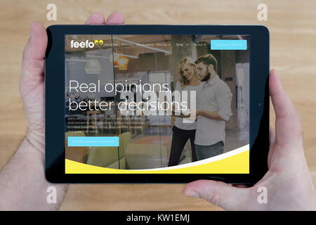 A man looks at the Feefo website on his iPad tablet device, shot against a wooden table top background (Editorial use only) Stock Photo