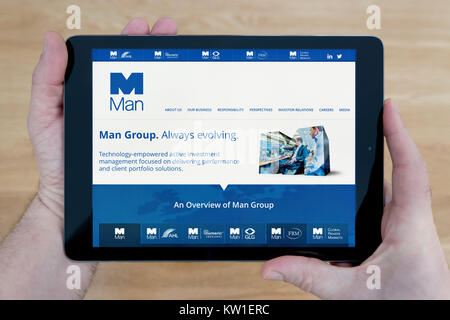 A man looks at the Man Group PLC website on his iPad tablet device, shot against a wooden table top background (Editorial use only) Stock Photo