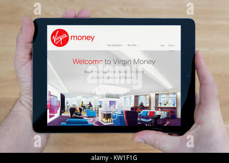 A man looks at the Virgin Money website on his iPad tablet device, shot against a wooden table top background (Editorial use only) Stock Photo
