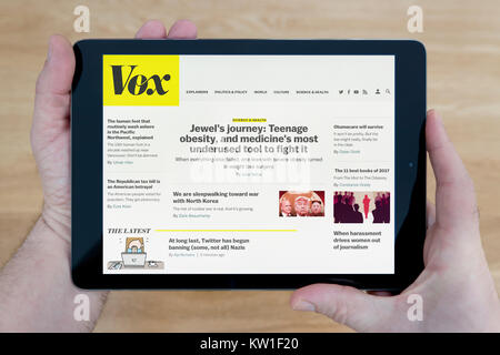 A man looks at the Vox website on his iPad tablet device, shot against a wooden table top background (Editorial use only) Stock Photo