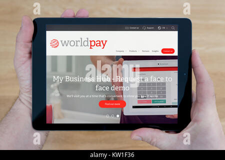 A man looks at the Worldpay website on his iPad tablet device, shot against a wooden table top background (Editorial use only) Stock Photo
