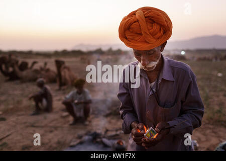 Scene at Pushkar Camel Fair, trader wearing turban lighting fire at twilight, Pushkar, Rajasthan, India Stock Photo