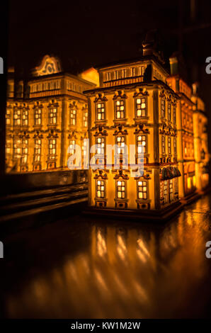 An illuminated partylite tealight miniature house on a wooden surface in front of the mirror Stock Photo