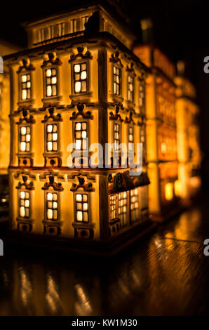 An illuminated partylite tealight miniature house on a wooden surface in front of the mirror Stock Photo