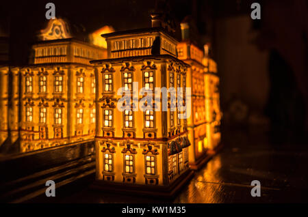 An illuminated partylite tealight miniature house on a wooden surface in front of the mirror Stock Photo