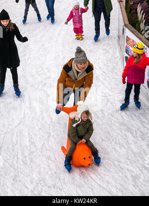 Edinburgh, Scotland, United Kingdom, 30th December 2018. Families with small children enjoying the New Year weekend ice skating in St Andrew Square. A parent pushes a child in a seal ice skating aid Stock Photo