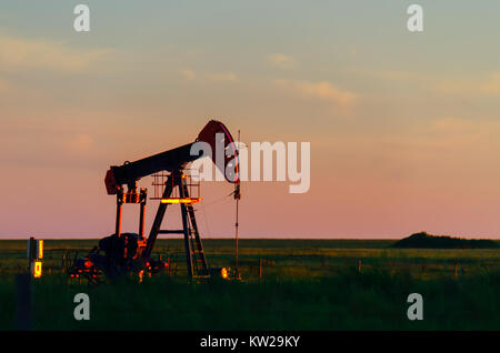 At sunset, oil pumps pour oil on a black field with a pond. Red glow in the background. Stock Photo