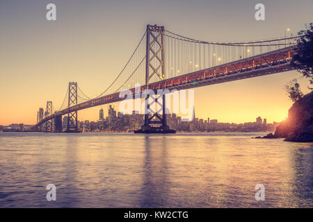 Classic panoramic view of San Francisco skyline with famous Oakland Bay Bridge illuminated in beautiful golden evening light at sunset in summer, San  Stock Photo