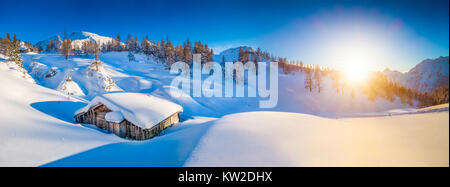 Panoramic view of beautiful winter mountain landscape with snow capped mountain cabin in the Alps in golden evening light at sunset Stock Photo