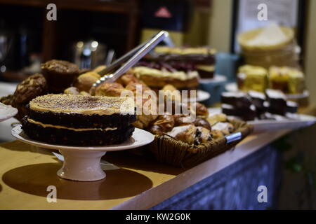Variety of baked goods on a counter in a cake shop with a layered chocolate sponge cake in the foreground Stock Photo