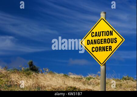 Yellow sign warning of dangerous corner against bright blue summer sky. Stock Photo