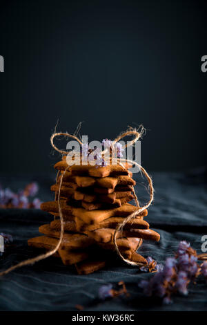 Tied stack of star shaped gingerbread cookies. Decorated with dried violet flowers, dark background. Stock Photo