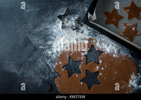 Christmas gingerbread star cookie cutter on flour, gingerbread dough with star shaped cutout and cookie star cut out of the dough in sheet pan. Stock Photo