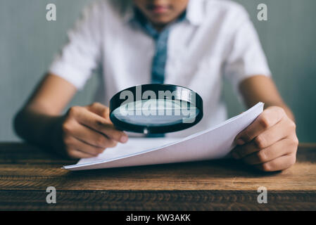 asian boy student looking at paper using magnifying glass. education concept Stock Photo