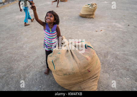 A little girl gets all excited looking at a airplane flyimng overhead as she manages a large gunny sack of dried fish. Stock Photo