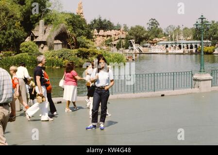 Tourist posing in front of a lagoon in the Disneyland theme park, with the attraction Big Thunder Mountain Railroad partially visible in the background, Anaheim, California, 1975. Stock Photo