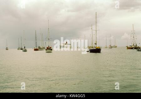 Cunard Line's Queen Elizabeth 2 cruise ship is visible in the distance across a stretch of water, with small sailboats in the foreground, on a cloudy day, 1975. Stock Photo