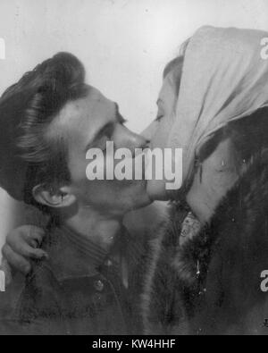 Two young lovers locked in a passionate kiss, the woman wearing a shawl and fur coat, with her hand resting on the man's neck, the man wearing a pompadour haircut, 1950. Stock Photo