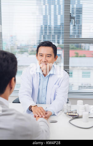 Male asian doctor comforting patient at consulting room Stock Photo